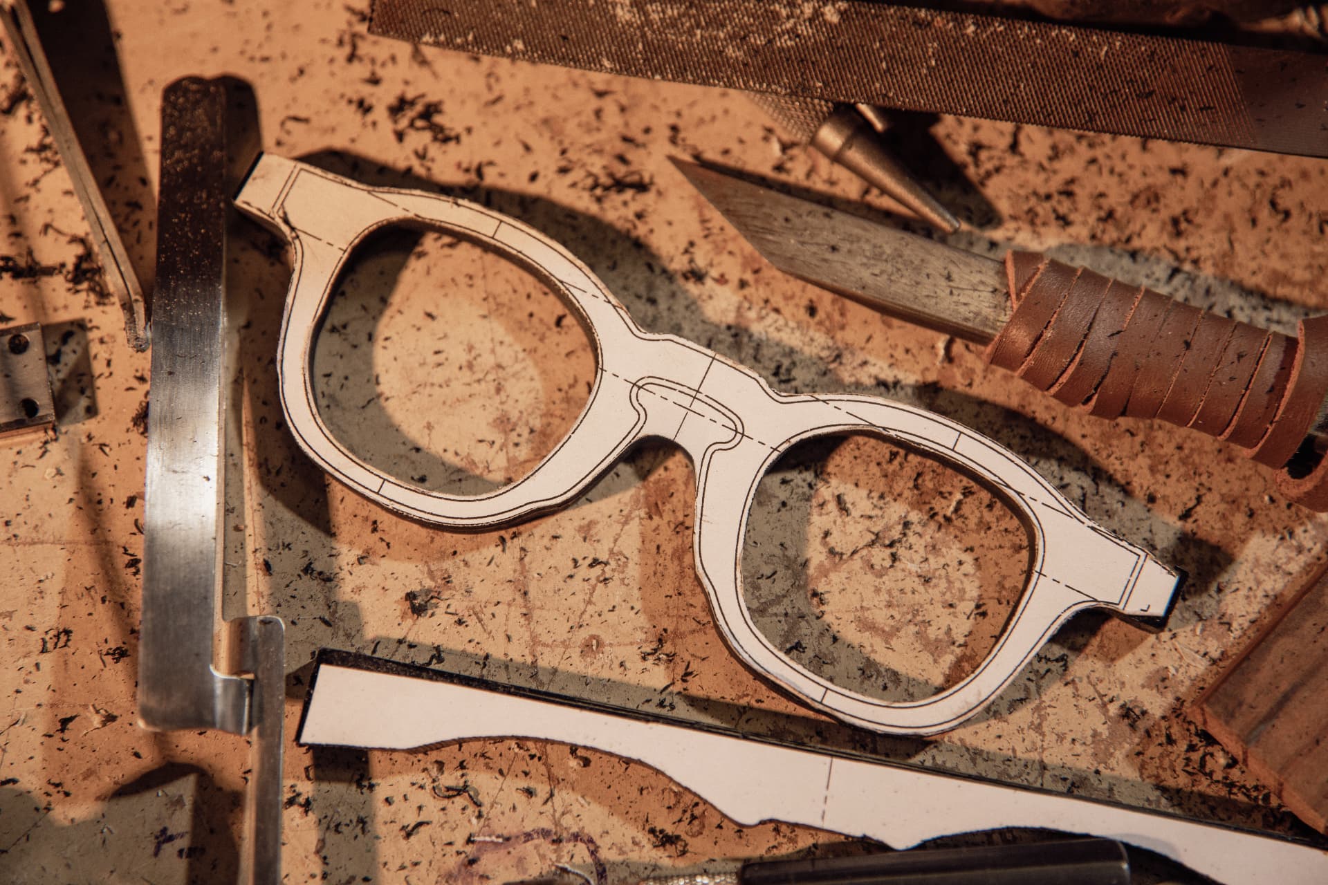 Cut-out frame on a paper template, with a file and a leather-handled knife on the atelier workbench.