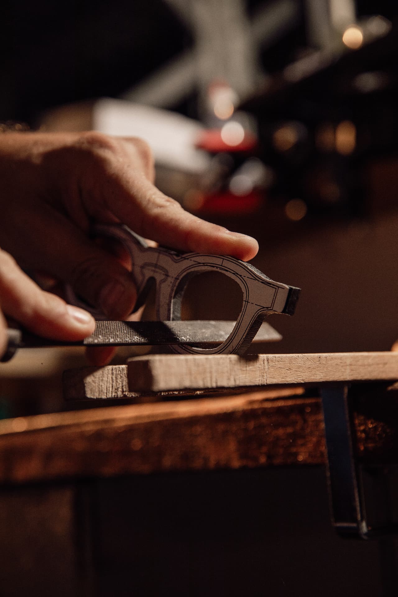 A lunetier's hands filing a bespoke frame on a wooden bench at the atelier in Rio de Janeiro.